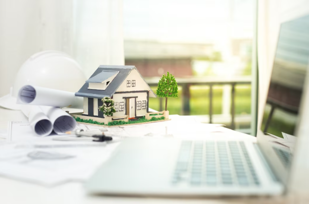 a side view of the opened laptop, the small house with trees near it, and papers on the table